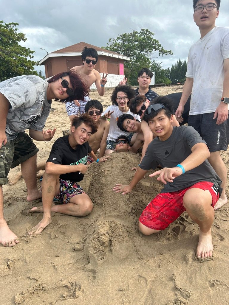 Friends crowded around a mound of sand on a beach