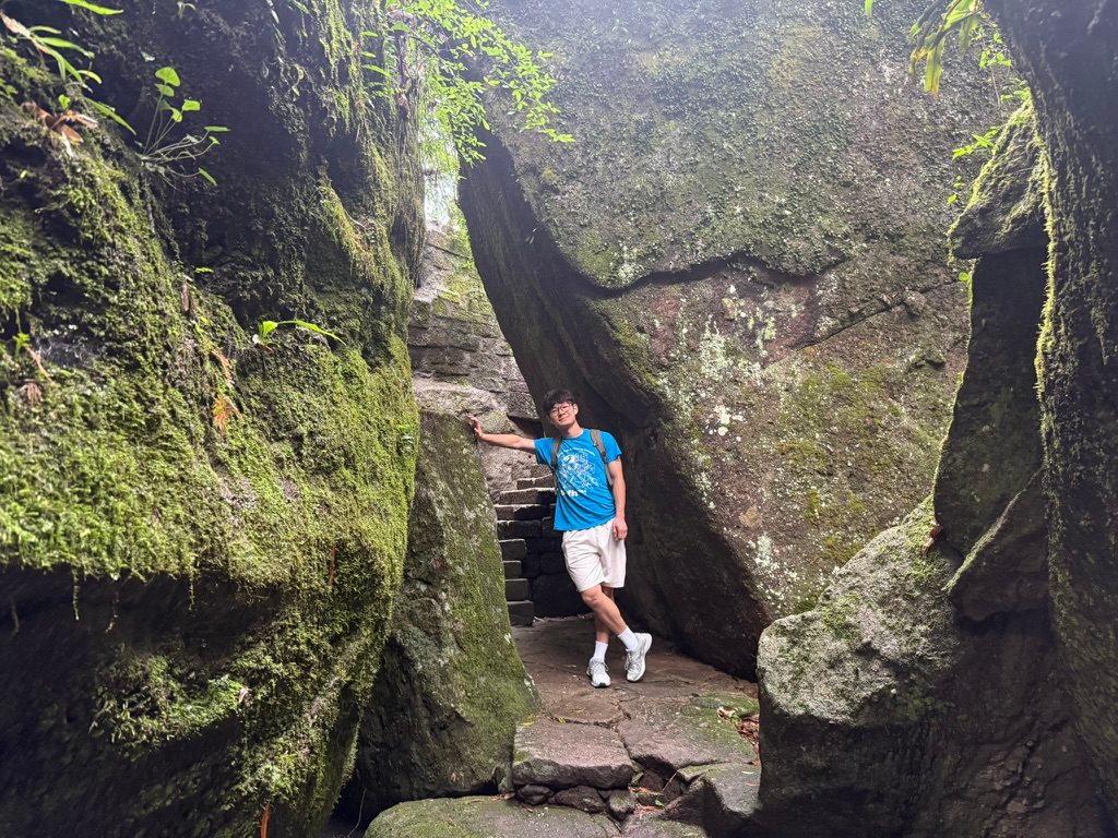 Junhao standing on stone steps between two moss-covered rock walls