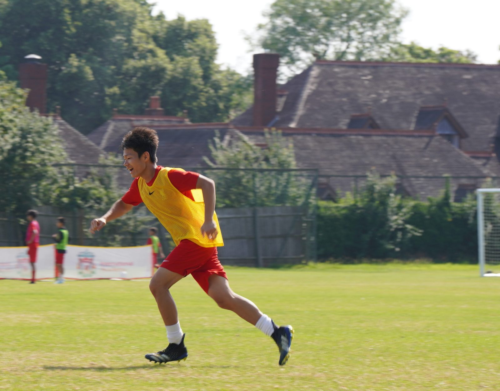 Junhao running on a soccer field in a yellow bib and red shorts